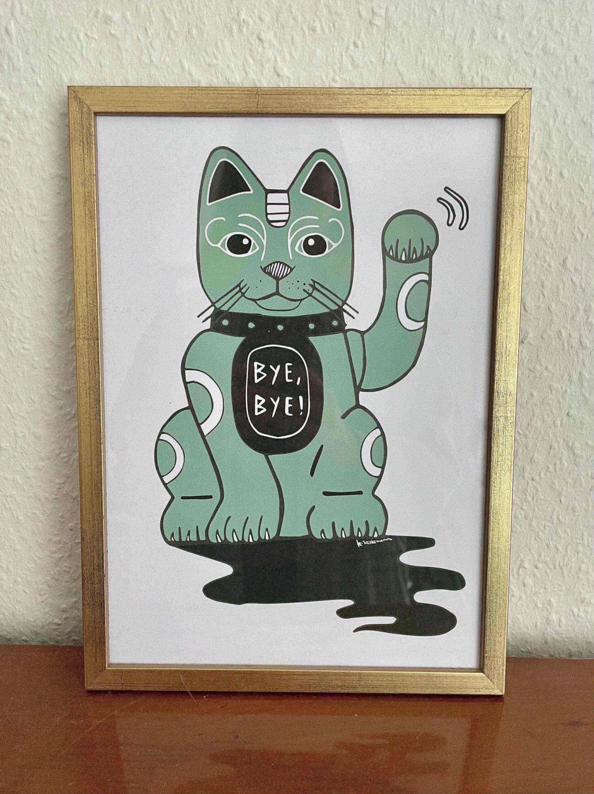 Lucky cat print with the words BYE BYE in a golden frame on a wooden table